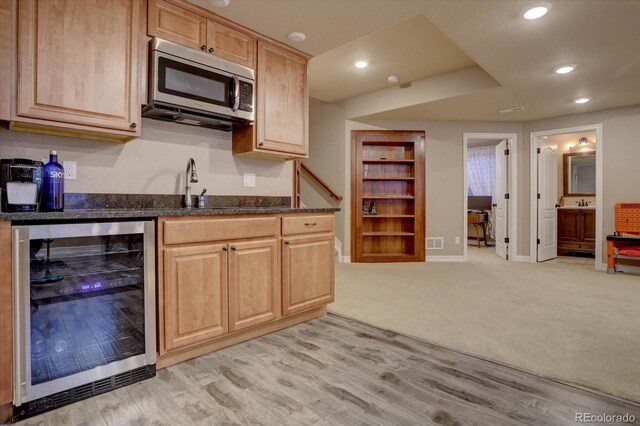 kitchen with light brown cabinets, dark stone counters, sink, wine cooler, and light colored carpet