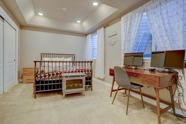 bedroom with a raised ceiling, light carpet, and a closet