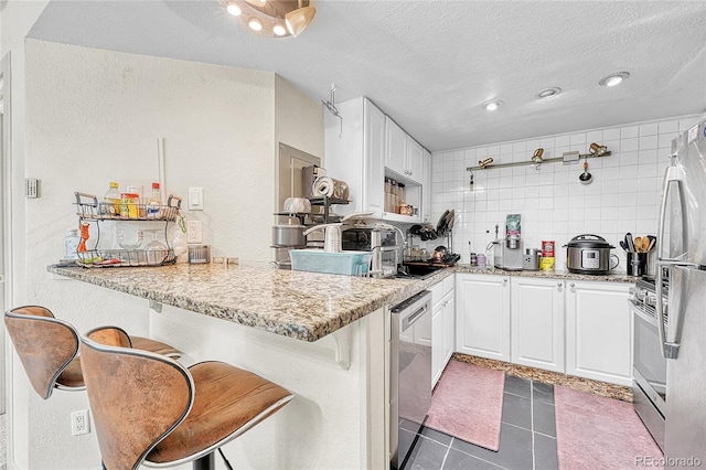 8701 Huron St Unit 211, Thornton, CO 80260 - kitchen with appliances with stainless steel finishes, a peninsula, white cabinets, tile patterned flooring, and a textured ceiling