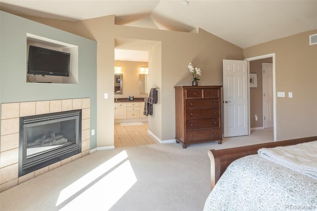 bedroom featuring a tile fireplace, lofted ceiling, light carpet, and connected bathroom