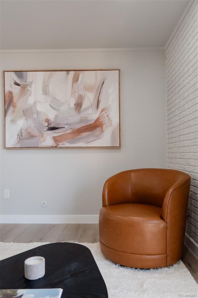 sitting room featuring wood finished floors, baseboards, brick wall, and ornamental molding