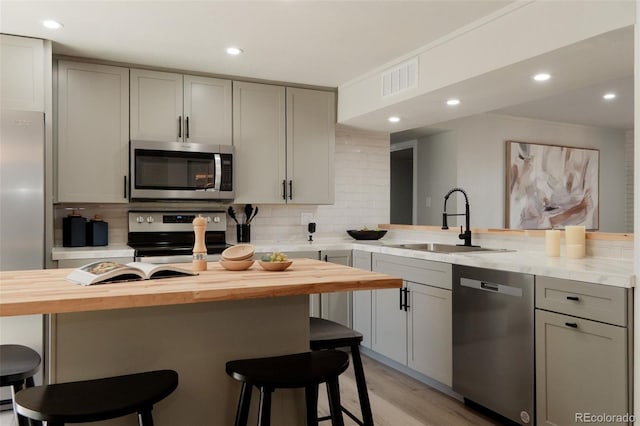 kitchen featuring gray cabinetry, decorative backsplash, a sink, appliances with stainless steel finishes, and wood counters