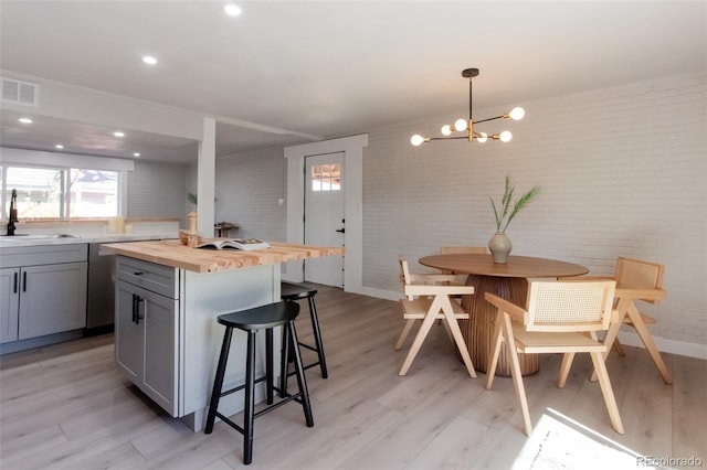 kitchen featuring visible vents, a sink, gray cabinetry, wood counters, and a kitchen breakfast bar