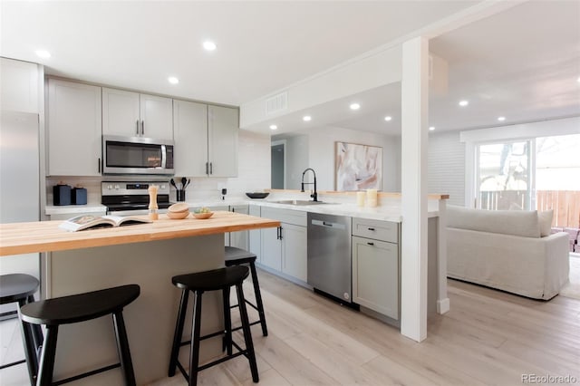 kitchen with a breakfast bar area, a sink, decorative backsplash, stainless steel appliances, and wood counters