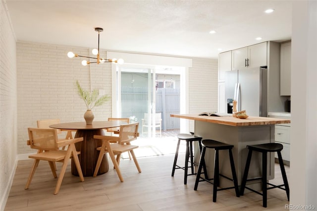 kitchen with fridge with ice dispenser, a kitchen bar, wood counters, brick wall, and a chandelier