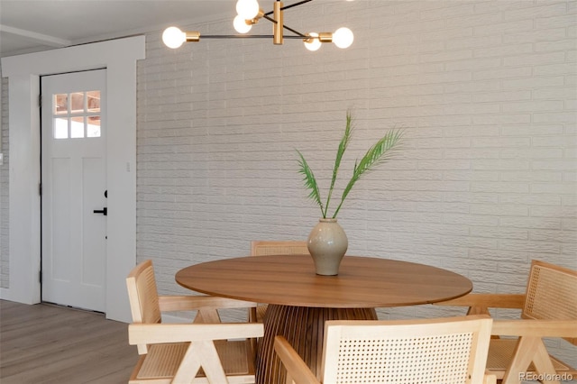 dining room with a notable chandelier, brick wall, and wood finished floors