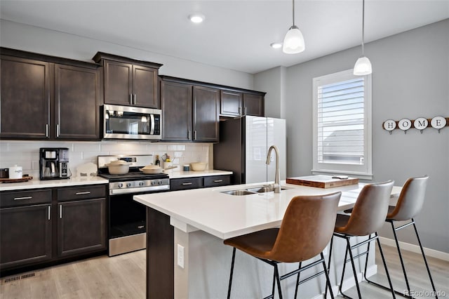 kitchen with a kitchen breakfast bar, pendant lighting, stainless steel appliances, light wood-type flooring, and a center island with sink