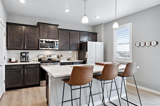 kitchen featuring pendant lighting, stainless steel appliances, decorative backsplash, and light hardwood / wood-style flooring