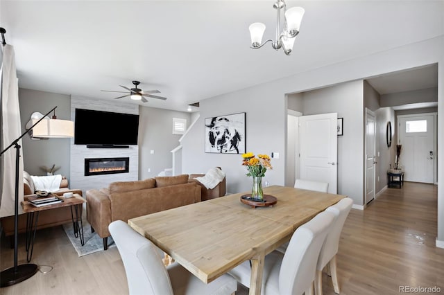 dining area featuring a wealth of natural light, ceiling fan with notable chandelier, a fireplace, and light hardwood / wood-style flooring