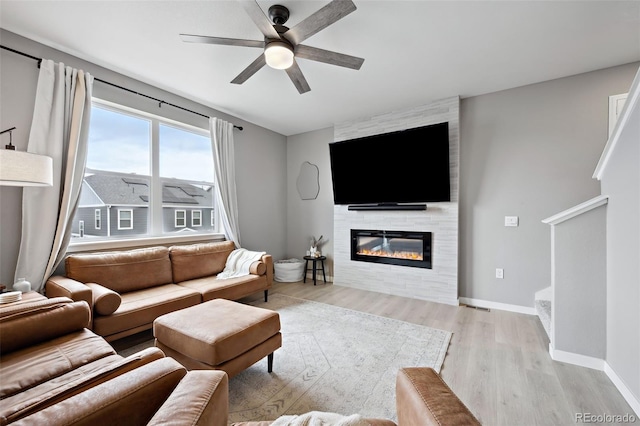 living room with ceiling fan, light hardwood / wood-style floors, and a large fireplace