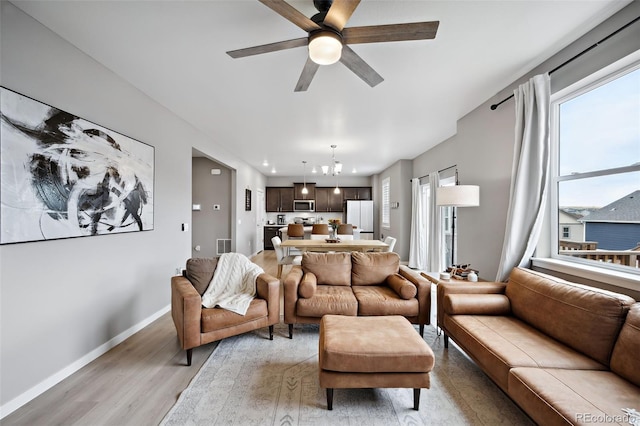 living room with ceiling fan with notable chandelier and light wood-type flooring