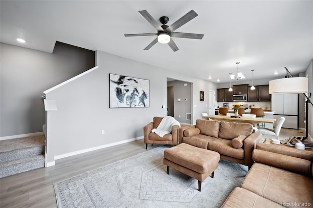 living room with light wood-type flooring and ceiling fan with notable chandelier