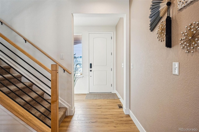 foyer entrance with stairway, visible vents, baseboards, light wood-style floors, and a textured wall