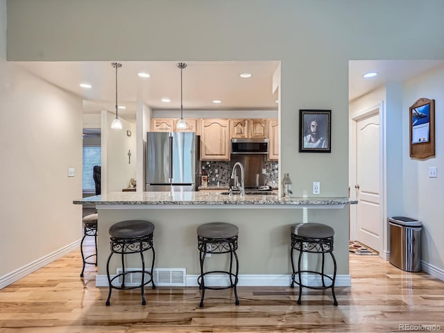 4063 S Cathay Ct, Aurora, CO 80013 - kitchen with appliances with stainless steel finishes, light brown cabinets, a kitchen breakfast bar, light wood-type flooring, and recessed lighting