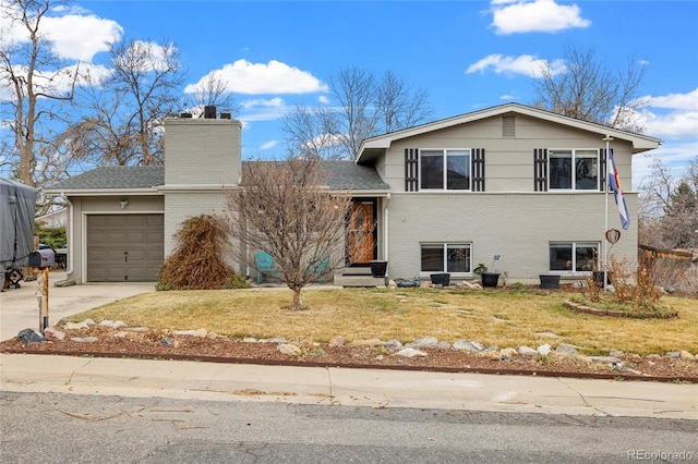 split level home featuring a front yard, driveway, a chimney, a garage, and brick siding