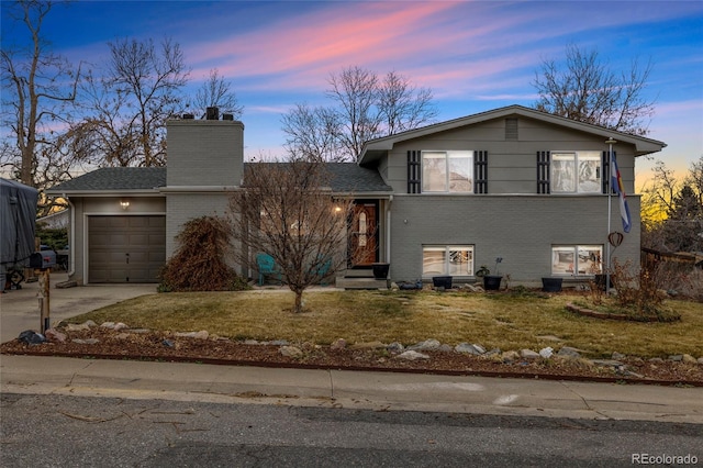 split level home featuring brick siding, concrete driveway, a chimney, a yard, and an attached garage