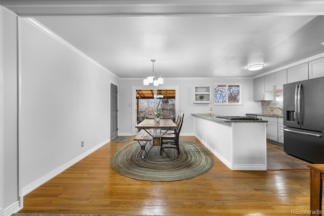 kitchen featuring wood finished floors, a peninsula, stainless steel refrigerator with ice dispenser, tasteful backsplash, and a chandelier