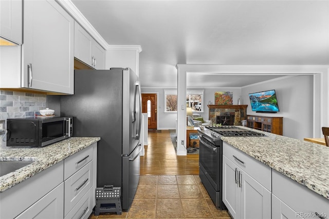 kitchen with black gas range oven, tasteful backsplash, light stone countertops, and ornamental molding