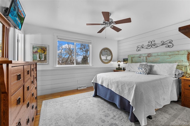 bedroom with visible vents, wooden walls, a wainscoted wall, wood finished floors, and a ceiling fan