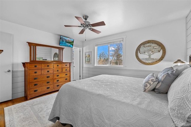 bedroom with ceiling fan, wood finished floors, and wainscoting