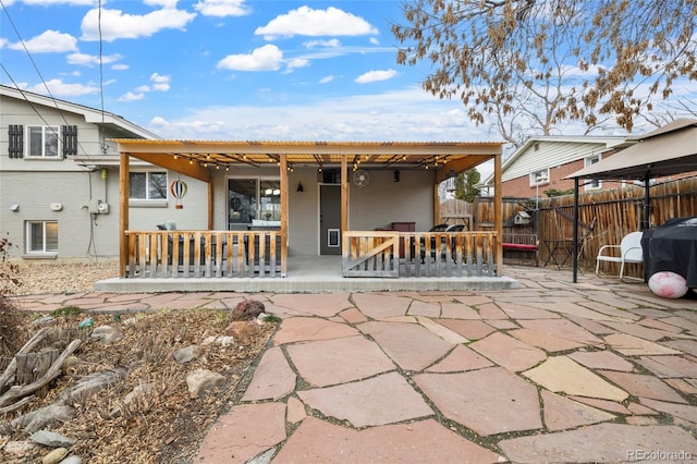 rear view of property with a porch, fence, and brick siding