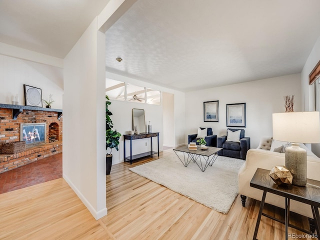 living room with baseboards, a brick fireplace, wood finished floors, and a ceiling fan