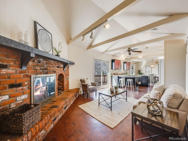 living room with a ceiling fan, lofted ceiling with beams, a fireplace, brick floor, and rail lighting