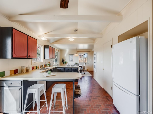 kitchen featuring beam ceiling, freestanding refrigerator, a peninsula, light countertops, and brick floor