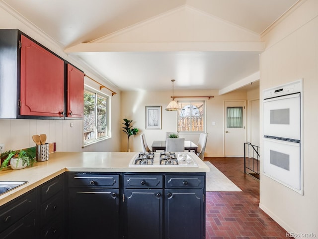 kitchen with light countertops, vaulted ceiling, a peninsula, brick floor, and white appliances