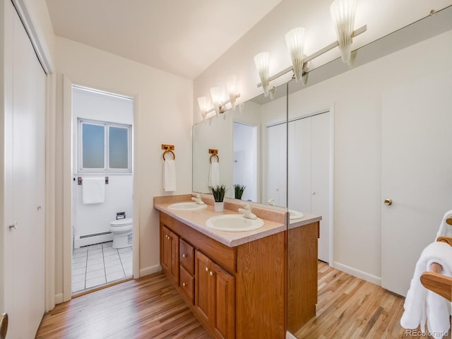 bathroom with a baseboard heating unit, toilet, wood finished floors, and a sink