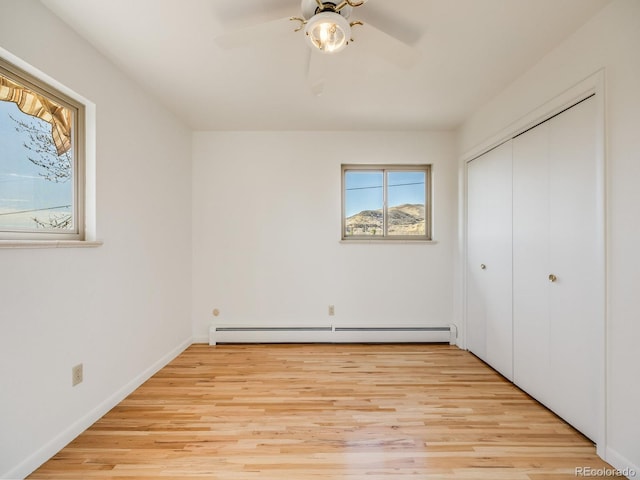 unfurnished bedroom with light wood-style floors, baseboard heating, a closet, and ceiling fan