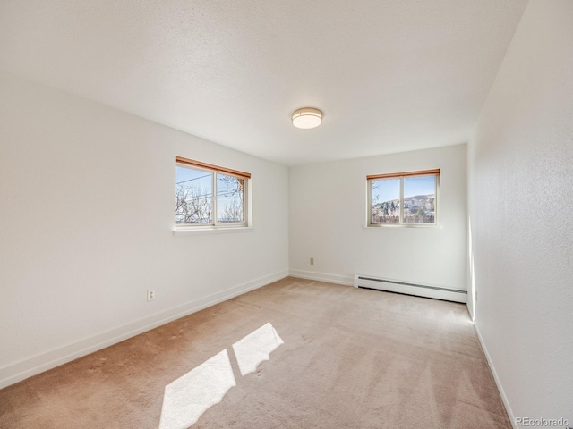 spare room with a baseboard heating unit, light carpet, and baseboards