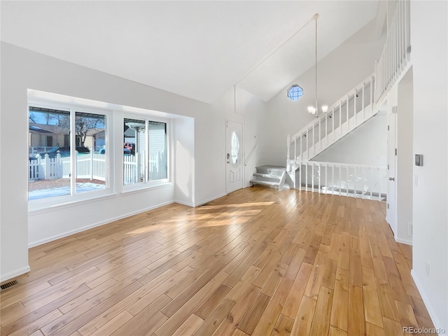 unfurnished living room with an inviting chandelier, high vaulted ceiling, and light hardwood / wood-style floors