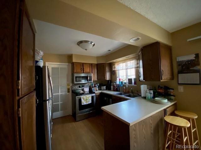 kitchen with light countertops, a peninsula, wood finished floors, appliances with stainless steel finishes, and a sink