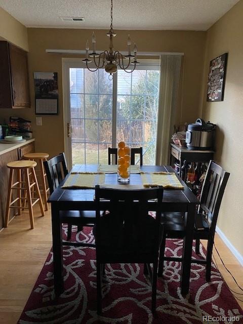 dining room featuring an inviting chandelier, a textured ceiling, light wood finished floors, and visible vents
