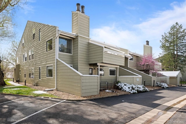 back of house featuring a chimney, fence, and uncovered parking