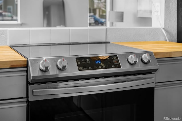 room details with gray cabinetry, tasteful backsplash, butcher block counters, and stainless steel electric stove
