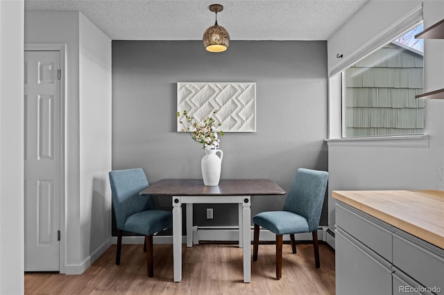 dining area featuring baseboards, light wood-style flooring, and a textured ceiling
