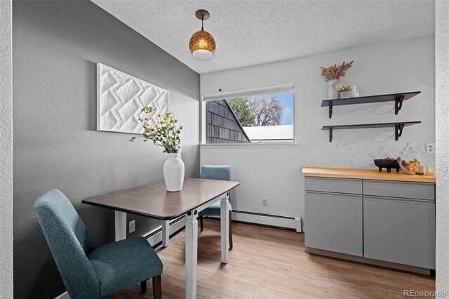 office space with a textured wall, light wood-style floors, baseboard heating, and a textured ceiling