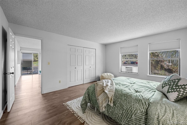 bedroom with wood finished floors, cooling unit, a closet, a textured ceiling, and baseboards