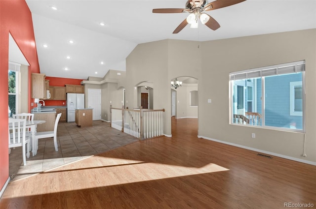 unfurnished living room with high vaulted ceiling, ceiling fan with notable chandelier, dark hardwood / wood-style floors, and sink