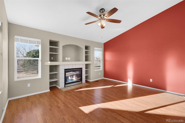 unfurnished living room with wood-type flooring, built in shelves, ceiling fan, and a fireplace