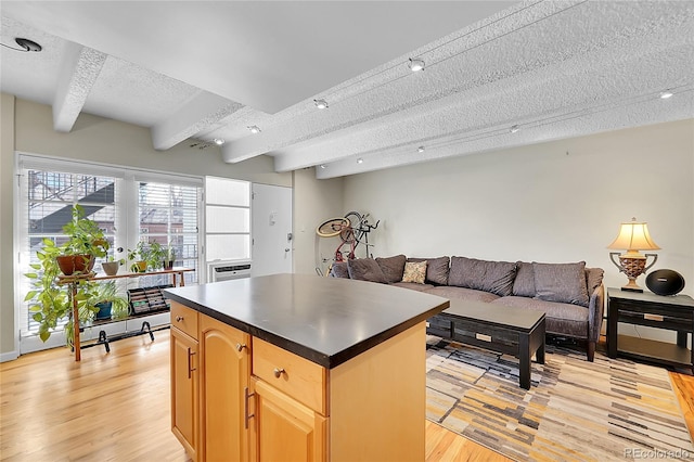 kitchen featuring beam ceiling, light wood-style flooring, a textured ceiling, dark countertops, and a center island