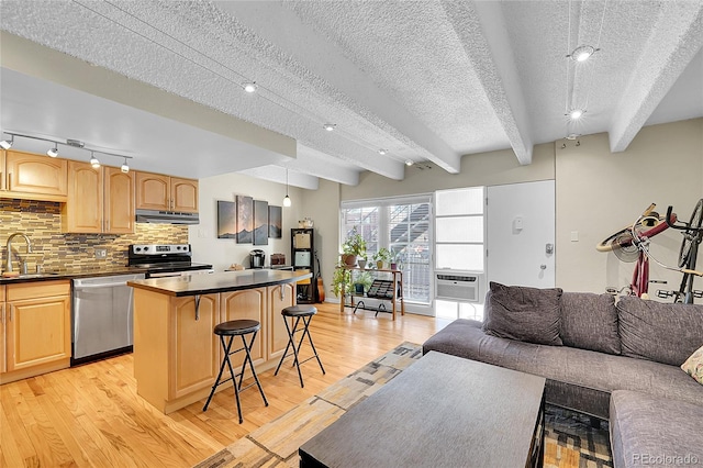 kitchen with dark countertops, under cabinet range hood, appliances with stainless steel finishes, a kitchen breakfast bar, and a sink