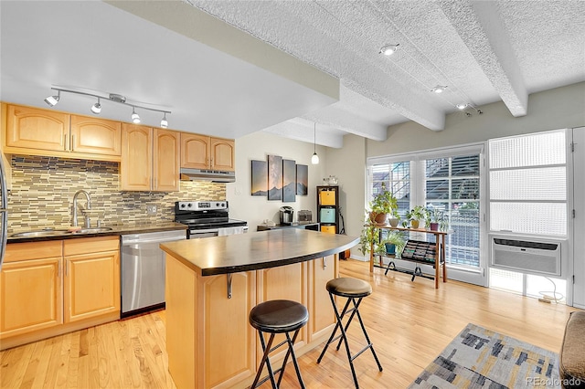 kitchen with dark countertops, stainless steel appliances, under cabinet range hood, and a sink