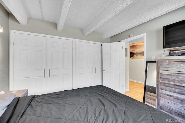 unfurnished bedroom featuring two closets, baseboards, beamed ceiling, wood finished floors, and a textured ceiling