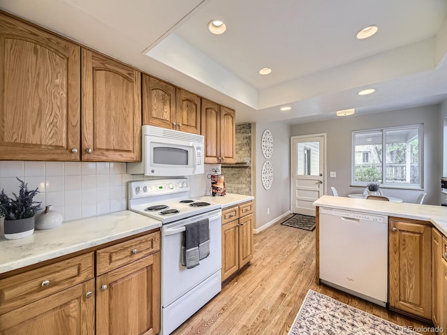 kitchen with white appliances, light hardwood / wood-style floors, tasteful backsplash, and a tray ceiling