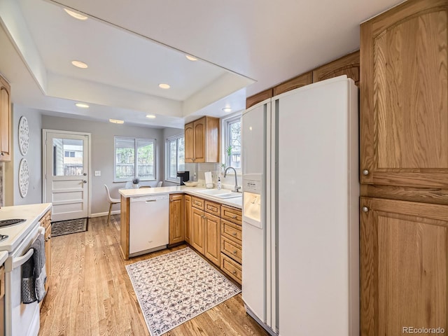 kitchen featuring sink, kitchen peninsula, plenty of natural light, light hardwood / wood-style floors, and white appliances