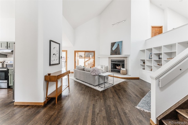 living area featuring high vaulted ceiling, a tile fireplace, baseboards, and wood finished floors