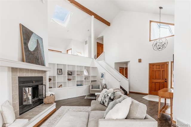 living area with baseboards, a tile fireplace, lofted ceiling with skylight, dark wood-type flooring, and a chandelier